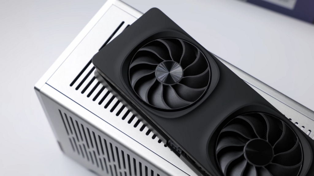 은색 PC 케이스 위에 놓인 검은색 인텔 Arc B580 그래픽카드의 두 냉각 팬