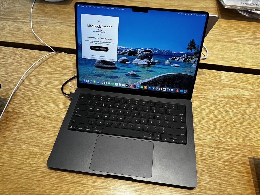 나무 전시대 위에 펼쳐진 스페이스 블랙 14형 MacBook Pro와 화면에 표시된 M5 칩 모델 안내