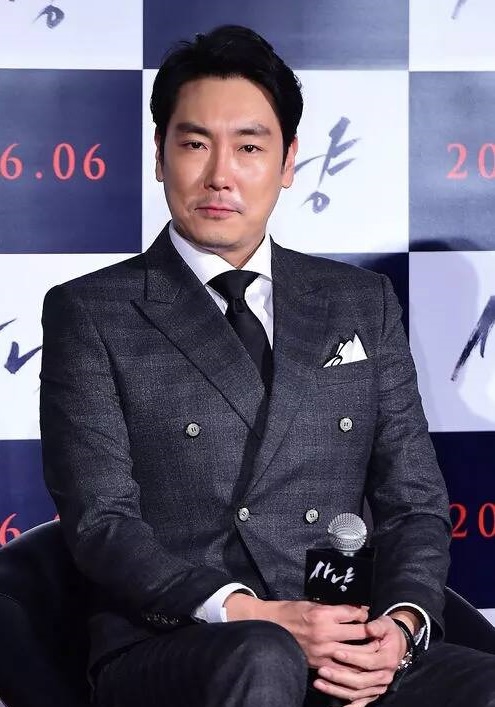 짙은 회색 정장을 입고 의자에 앉아 마이크를 들고 있는 조진웅