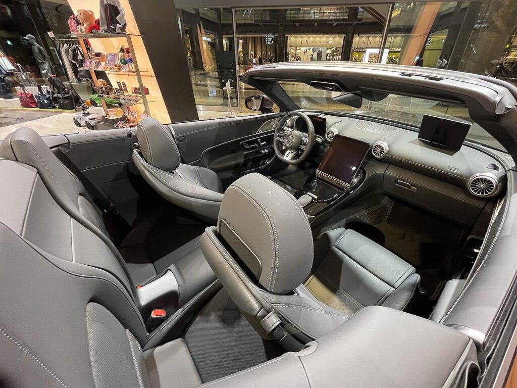 지붕을 연 메르세데스 AMG SL 43의 실내로, 앞좌석 뒤 작은 뒷좌석과 세로형 중앙 화면, 원형 송풍구가 보인다.